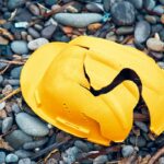 Cracked work helmet on the floor covered with pebble stones. Concept of work accident.